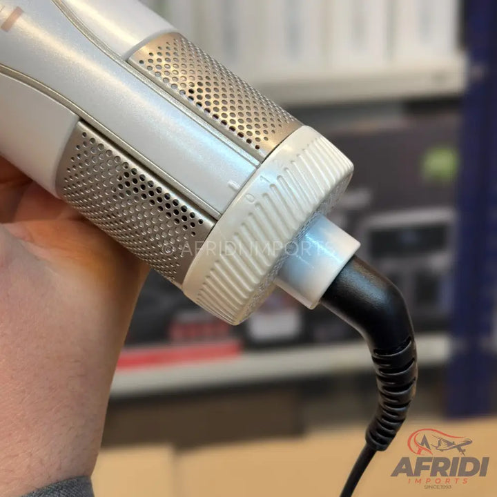 A white and silver hair styler with a ribbed rotating collar and a black power cord.