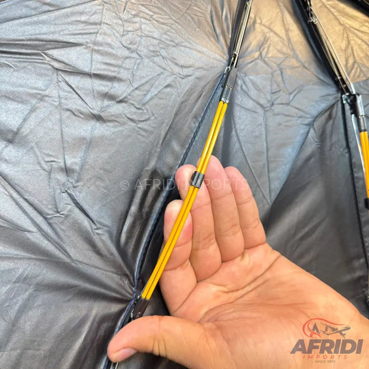 A hand holding up the yellow fiberglass pole and black fabric of a new product, likely a tent or umbrella.