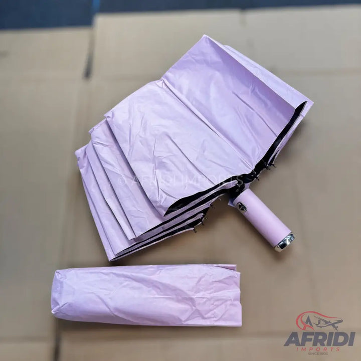 A light purple compact folding umbrella, partially open, with its matching storage sleeve.
