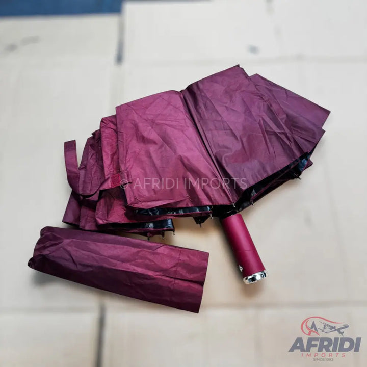 A partially folded burgundy umbrella with a matching sleeve.