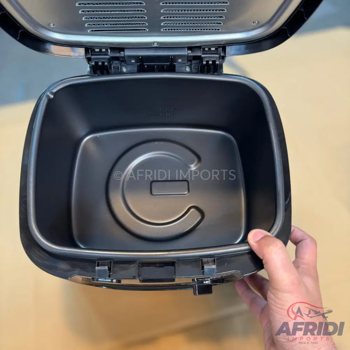 An opened black air fryer with an empty cooking basket.