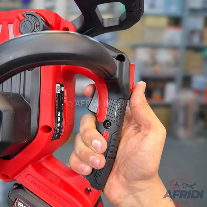 A hand holding a red and black cordless electric chainsaw.