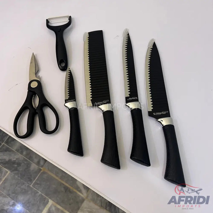 A set of black-handled kitchen knives with serrated blades, a peeler, and kitchen shears.