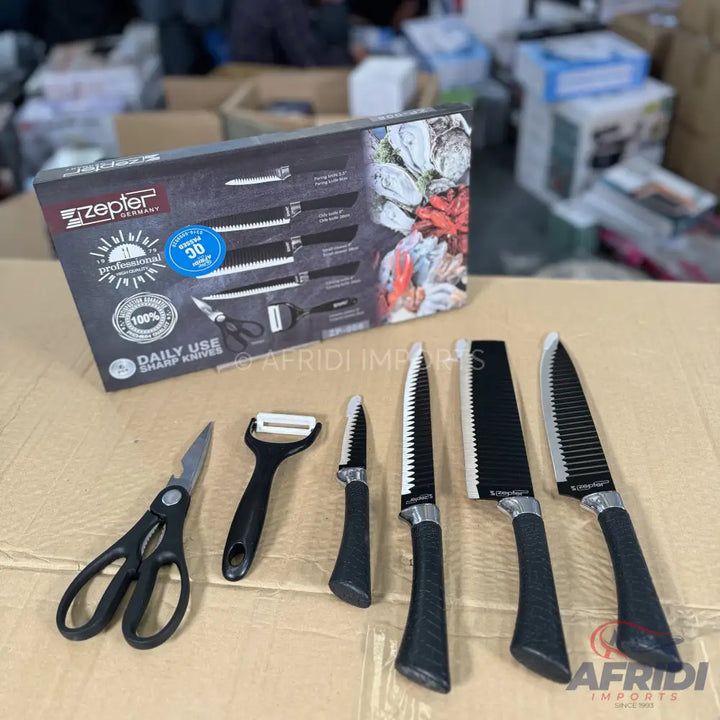 A set of black-handled kitchen knives, a peeler, and scissors in packaging.